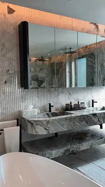 Grey veined stone is used for the vanity and its surrounding surfaces, alongside large mirrors and a clean vanity composition.