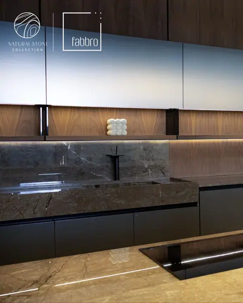 Dark stone with light veining is used for the kitchen countertop and splashback, alongside light cabinetry and warm timber finishes.