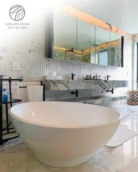 Pale veined stone is used for the bathroom walls and floor, alongside a freestanding white bath and soft lighting.