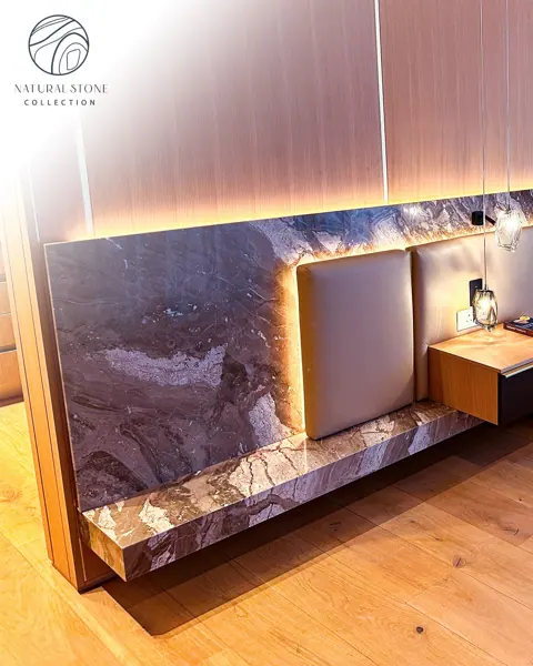 Violet and cream veined stone is used for the headboard wall and bedside setting, alongside vertical timber detailing and warm concealed lighting.
