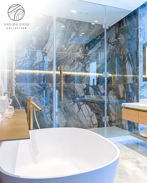 Blue stone with golden veins is used for the bathroom walls and floor, alongside a freestanding white bath and soft lighting.
