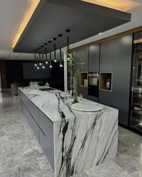 White marble with grey veining is used for the kitchen island and work surfaces, alongside dark cabinetry and warm timber details.