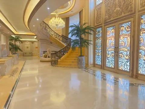 Soft cream stone is used for the entrance floor and architectural details, alongside a sweeping staircase and flowing architectural lines.