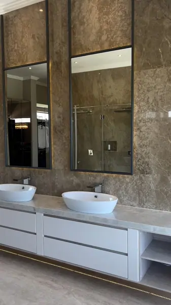 Rich brown veined stone is used for the vanity and its surrounding surfaces, alongside large mirrors and a clean vanity composition.