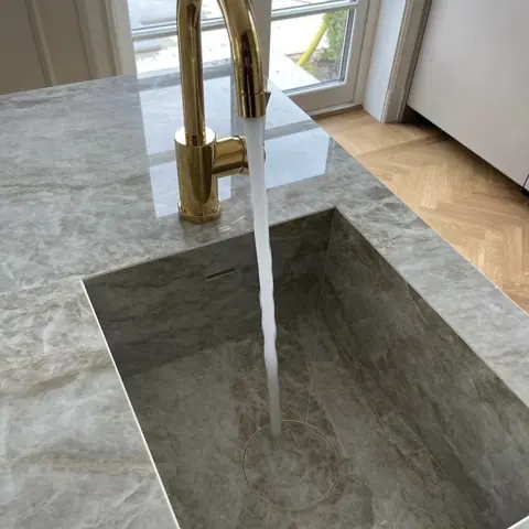 Grey veined stone is used for the vanity and its surrounding surfaces, alongside warm metallic details and carefully placed lighting.