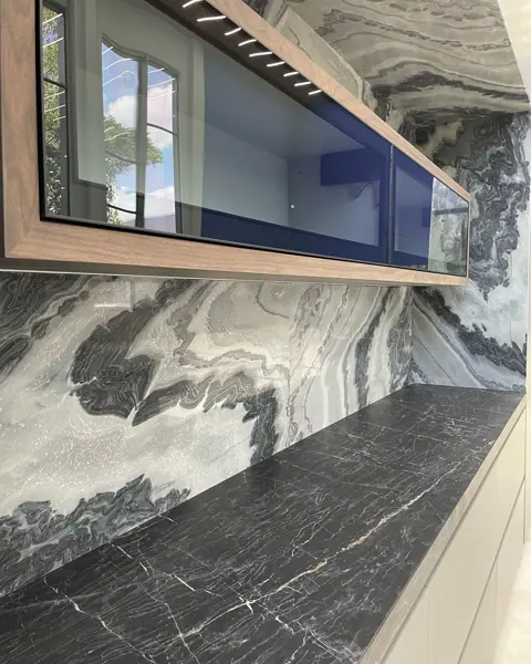 Grey veined stone is used for the kitchen countertop and splashback, alongside tall windows and a bright neutral interior.