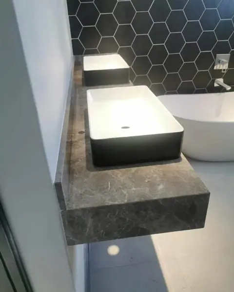Grey veined stone is used for the vanity and its surrounding surfaces, alongside clean architectural lines and contemporary fittings.