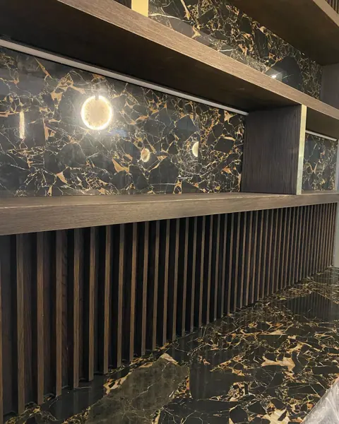 Black stone with golden veining is used for the bar counter and backdrop, alongside shelving and warm ambient lighting.
