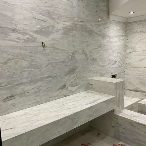 Stone with flowing linear bands is used for the bathroom walls and floor, alongside clean architectural lines and contemporary fittings.