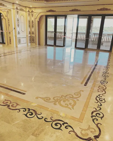 Warm beige natural stone is used for the entrance floor and architectural details, alongside contrasting borders and a carefully composed floor pattern.