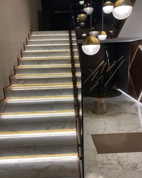 Pale veined stone is used for the stair treads and landings, alongside a golden glow and contrasting dark finishes.