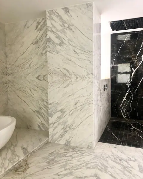 Stone with mirrored veining is used for the bathroom walls and floor, alongside dark taps and a sculptural basin.