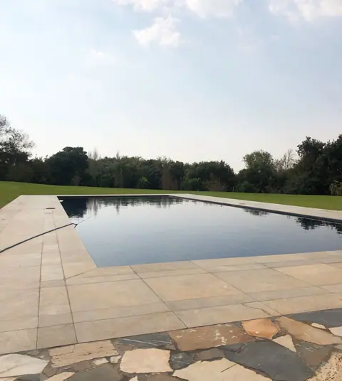 Warm beige natural stone is used for the poolside terrace, alongside garden views and relaxed outdoor seating.