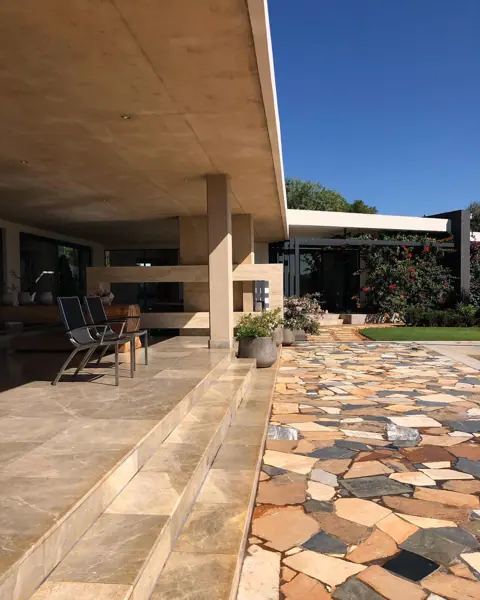 Rustic stone with natural variation is used for the terrace paving, alongside timber beams and a sheltered entertaining area.