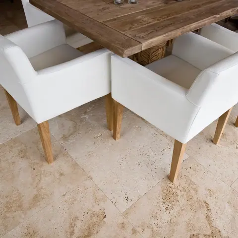 Soft cream stone is used for the floor throughout the room, alongside white dining chairs and a light interior palette.