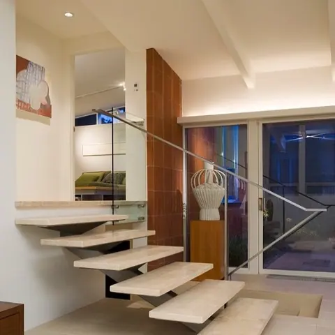 Pale veined stone is used for the stair treads and landings, alongside glass balustrades and generous daylight.