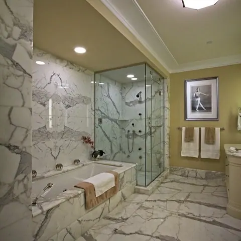 Pale veined stone is used for the bathroom walls and floor, alongside classical mouldings and decorative lighting.