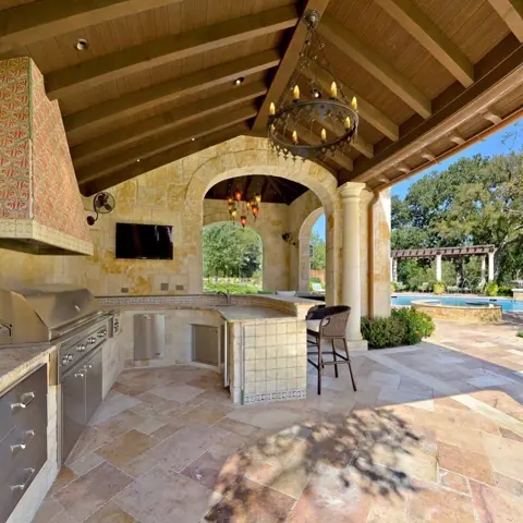 Warm beige natural stone is used for the terrace paving, alongside arched openings and a traditional interior palette.
