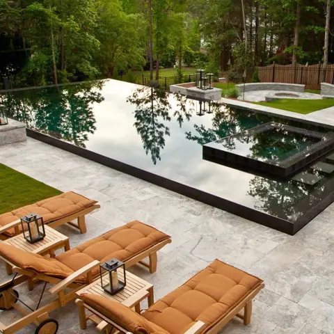 Pale veined stone is used for the poolside terrace, alongside garden views and relaxed outdoor seating.