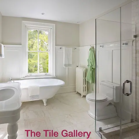 White marble with grey veining is used for the bathroom walls and floor, alongside tall windows and a bright neutral interior.