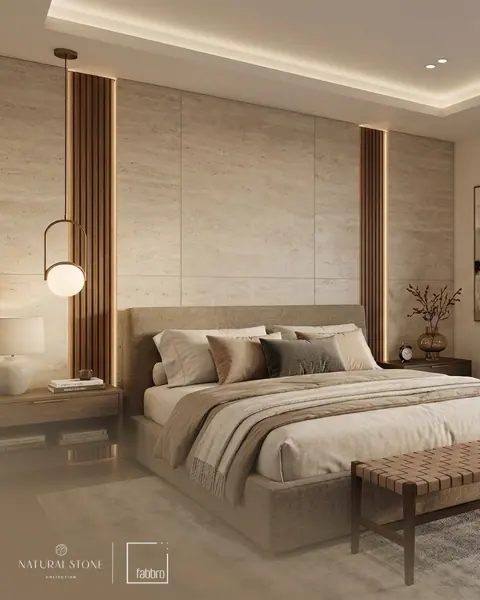 Pale stone panels form a full-height backdrop to the bed, balanced by timber details, soft furnishings and warm vertical lighting.