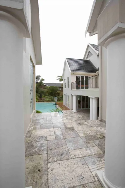 Stone paving continues past white columns into an open courtyard, where mixed tones give the outdoor surface a relaxed, established character.